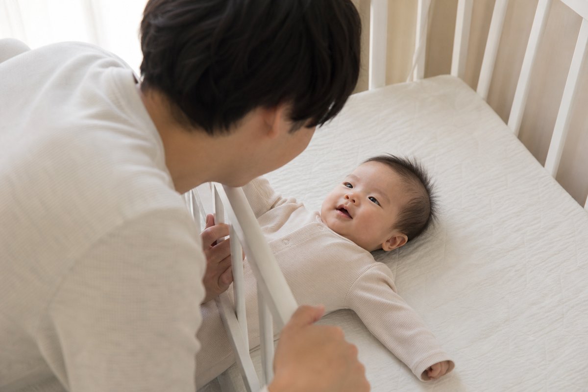 ベビーベッド越しに赤ちゃんを見守る父親